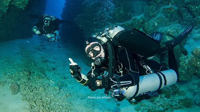 Divers exploring underwater cave, giving thumbs up.